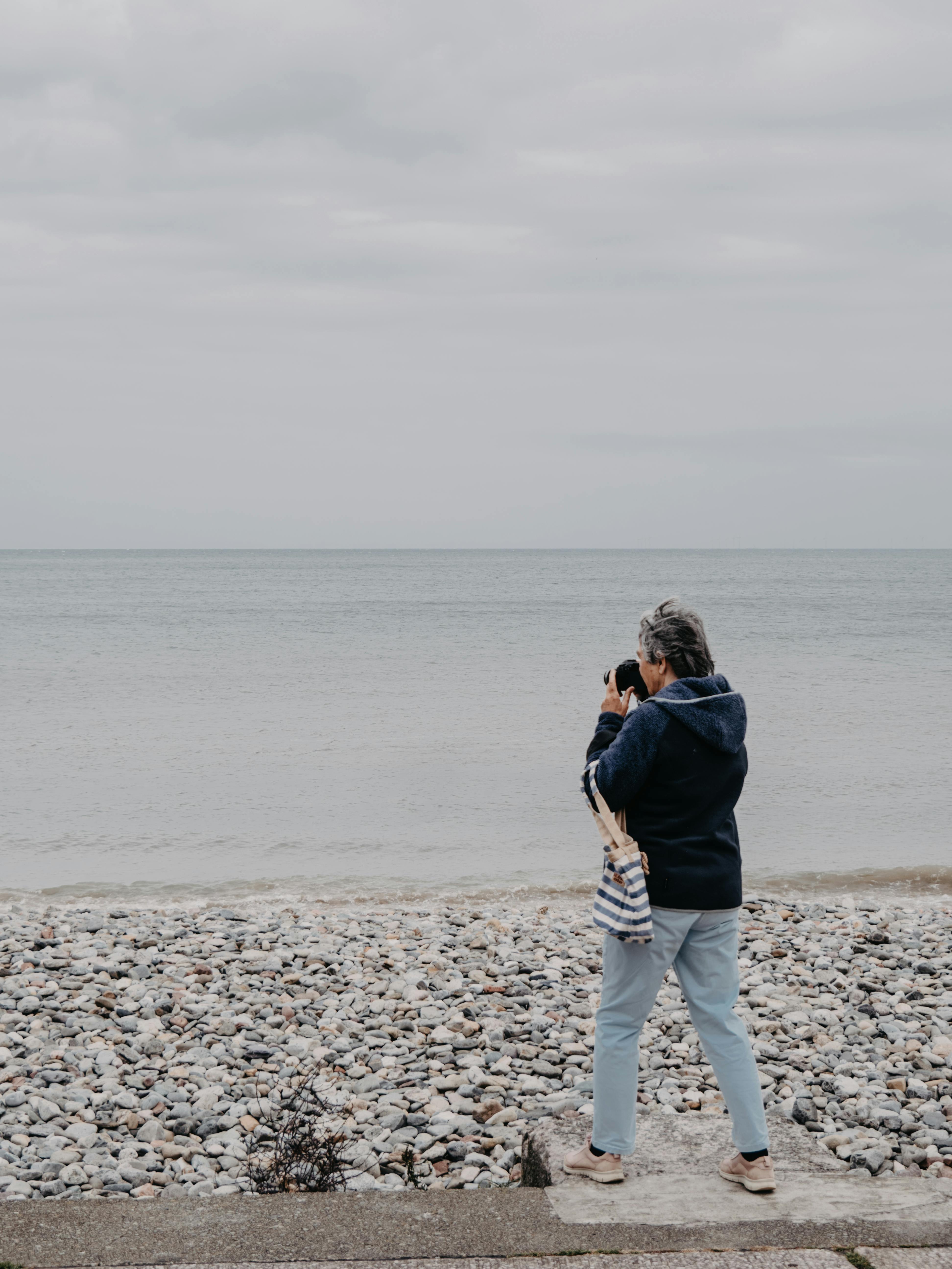 Senior woman takes photos at Llandudno beach, Wales on an overcast day.