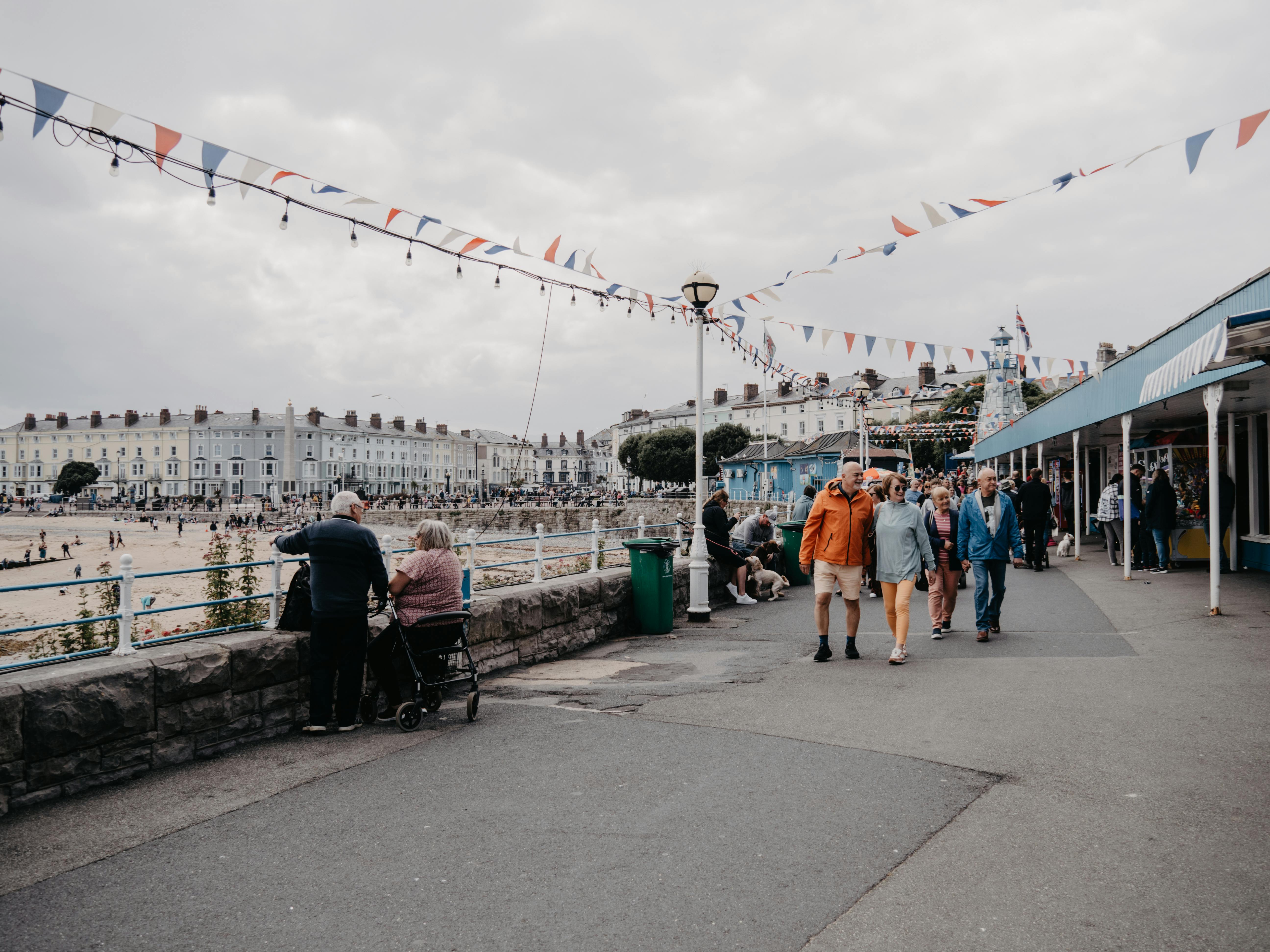 A bustling scene at Llandudno promenade with visitors, stalls, and beachfront views in Wales.