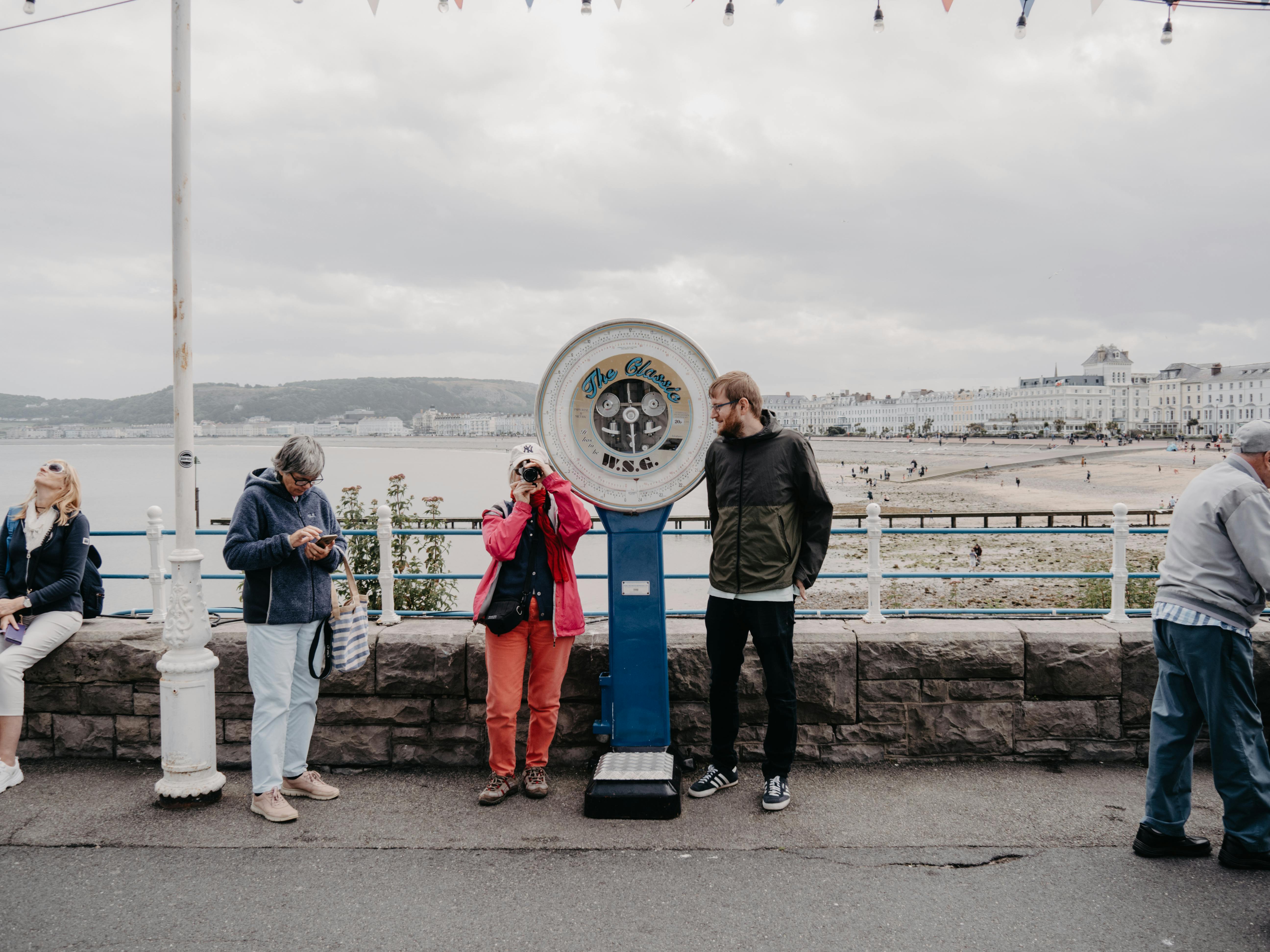 Lively scene on Llandudno promenade featuring people and a vintage scale.