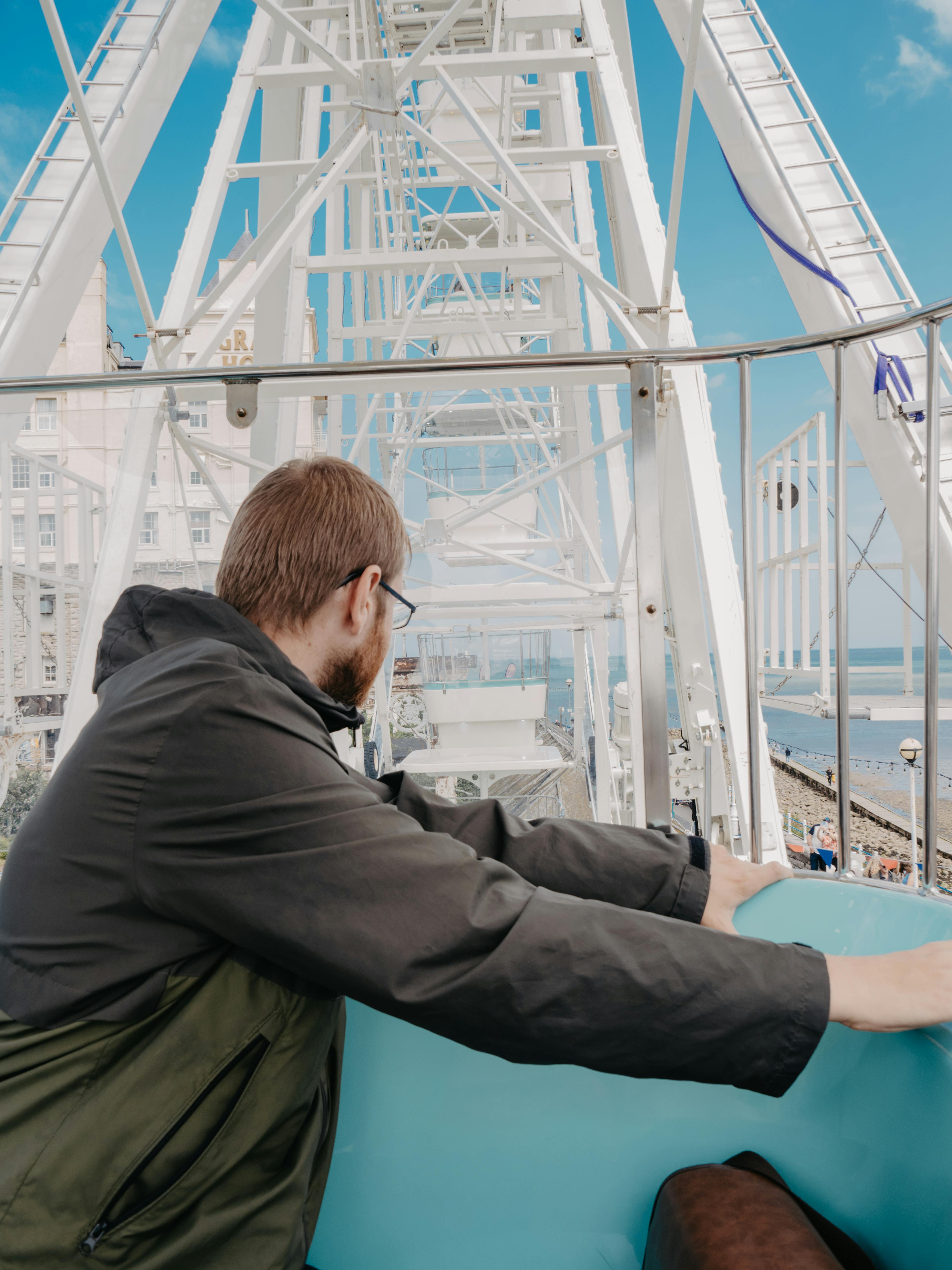 A man enjoys a scenic ride on a Ferris wheel in Llandudno, Wales, with coastal views.