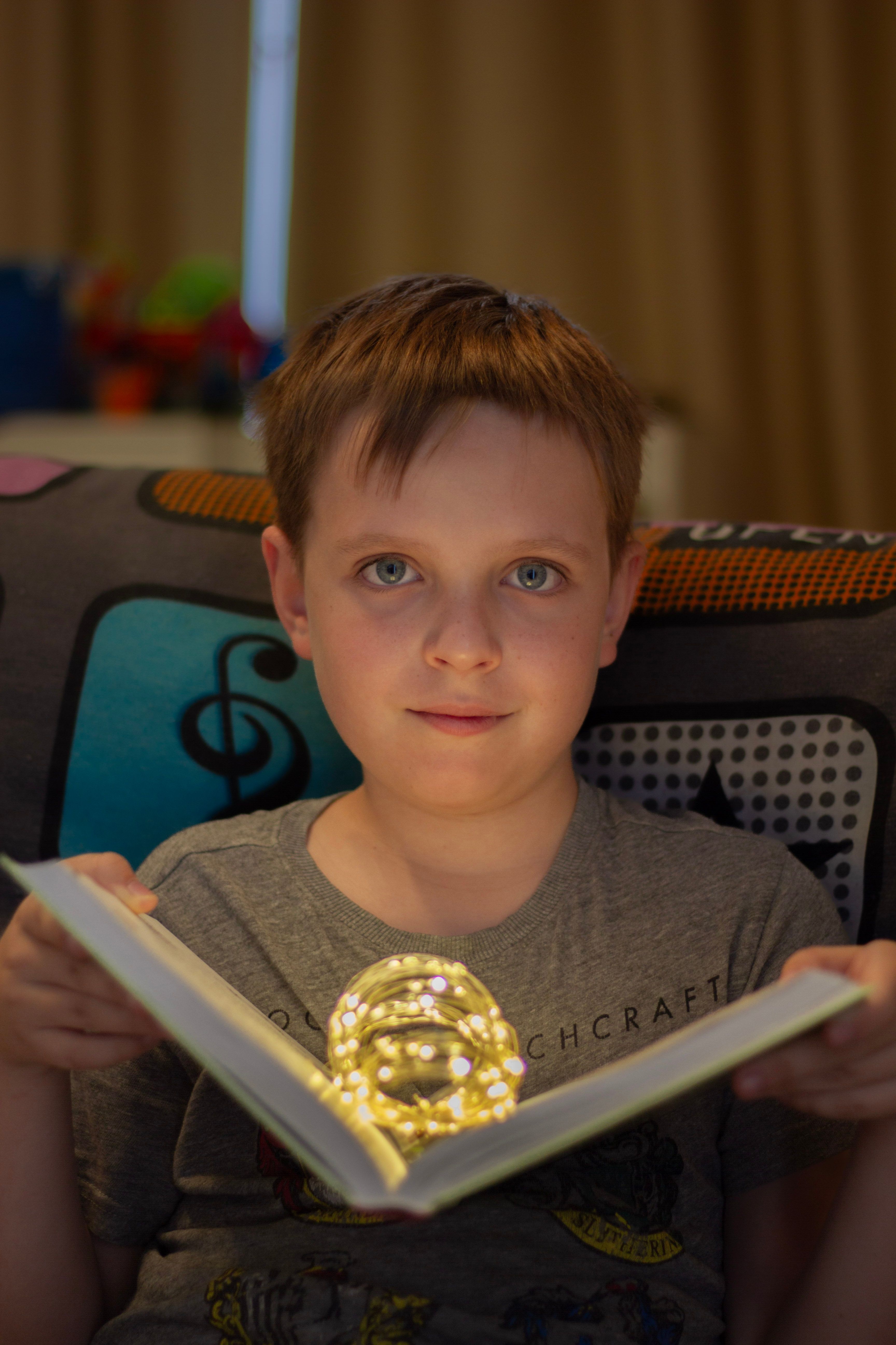 A child with brown hair reading a book illuminated by a magical light, creating a cozy indoor atmosphere.