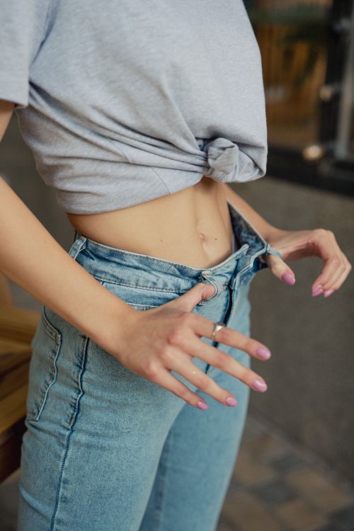 Free A woman in a t-shirt adjusting her blue jeans with focus on hands and waist. Stock Photo