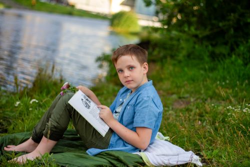 Free A young boy enjoys reading outdoors by the river on a warm summer day. Stock Photo