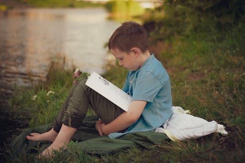 Boy Sitting on Riverbank and Reading
