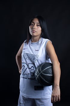 Young woman in sportswear holding basketball against black background.