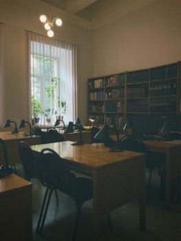 Quiet library with wooden tables, chairs, and bookcases lined with books.