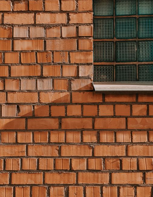 Detailed view of a brick wall with glass block window, showcasing urban architecture.