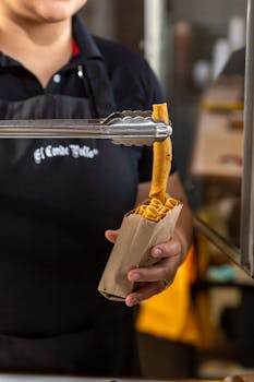 Vendor holding crispy spring rolls using tongs, ready for takeaway at a food stall.