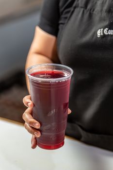 Close-up of a refreshing hibiscus drink in a plastic cup held by a person in a restaurant.