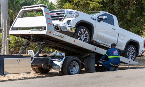 Bakkie Hire with Driver โ Tow truck operator loading white GMC pickup truck on street in daytime.