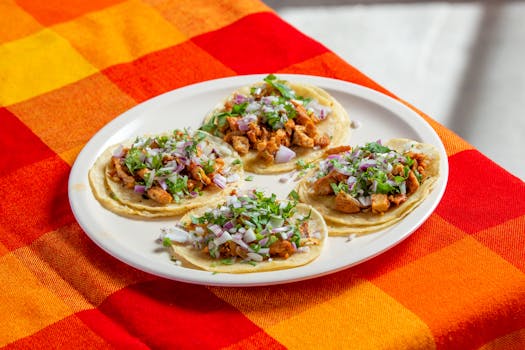 Four homemade chicken tacos garnished with onions and cilantro, served on a colorful tablecloth.