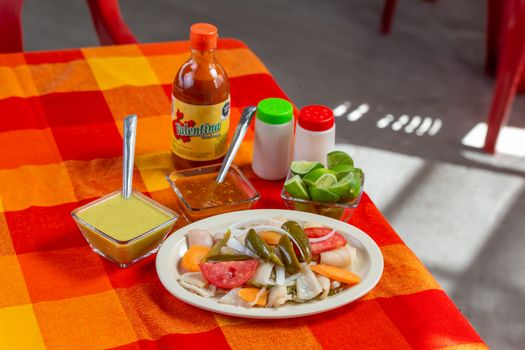 Colorful Mexican ceviche served with hot sauce, lime, and salsas on a vibrant tablecloth.