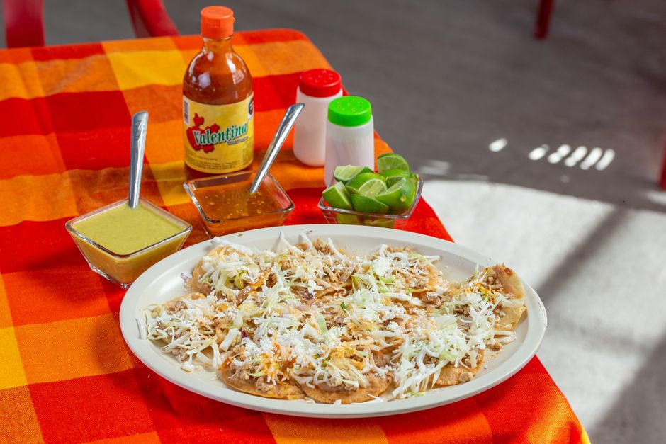 A glass bottle of deep red Mexican hot sauce next to dried guajillo and árbol chiles and a small dish of the sauce for dipping.