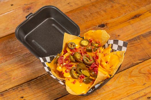 Delicious nachos topped with cheese, jalapenos, and bacon in a checkered takeout box.