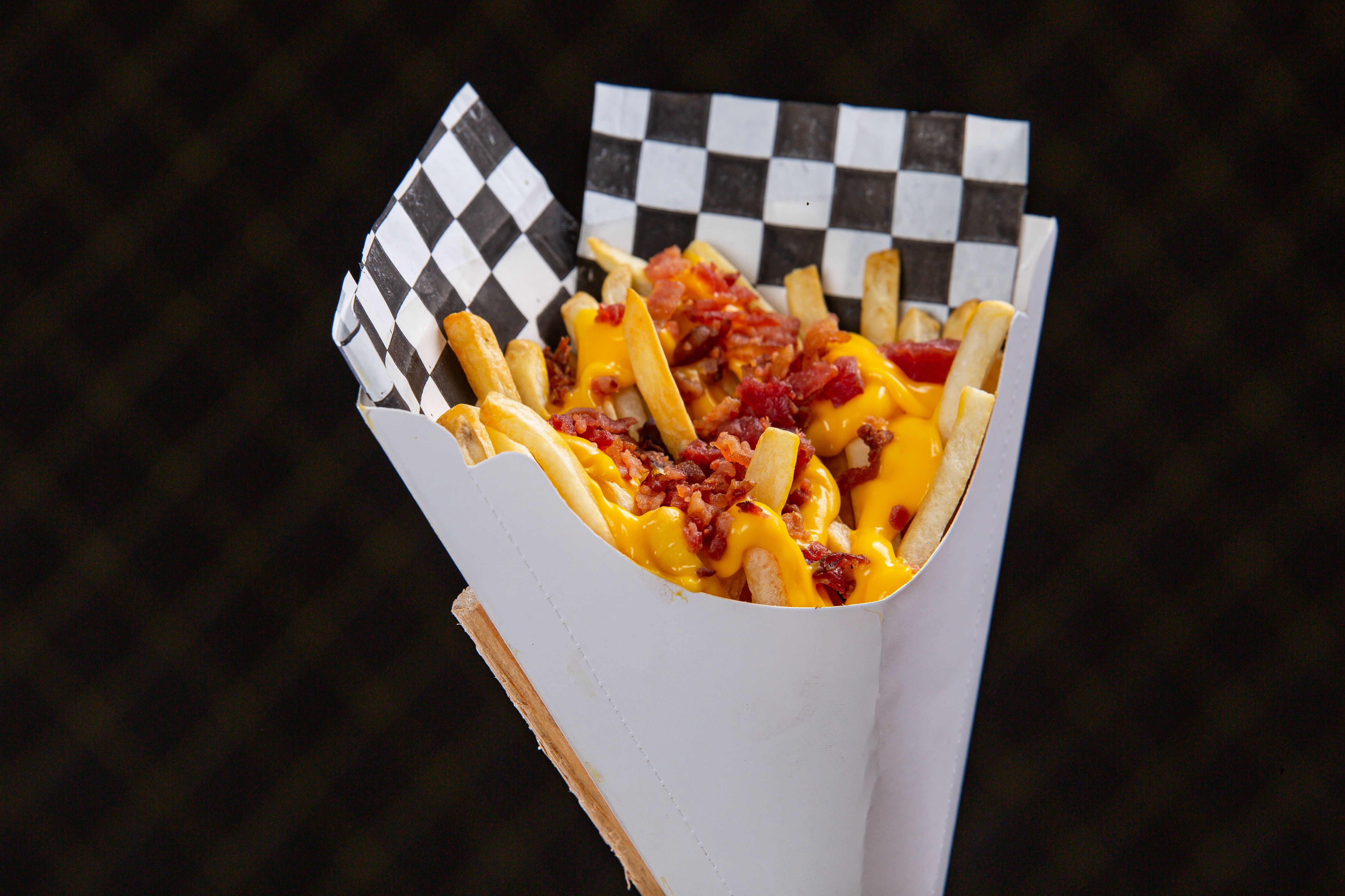 paper cone of thick cut fries with remoulade sauce on a steel counter at a hot dog stand