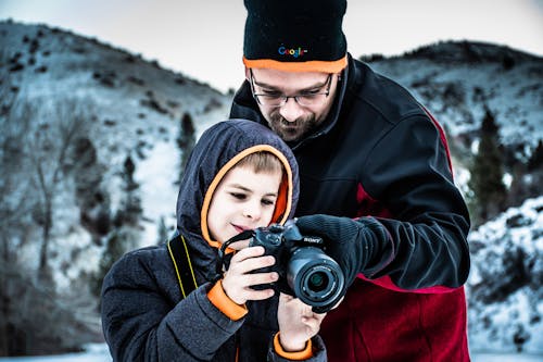 Man Standing Beside Boy While Holding Dslr Camera in Selective Focus Photography