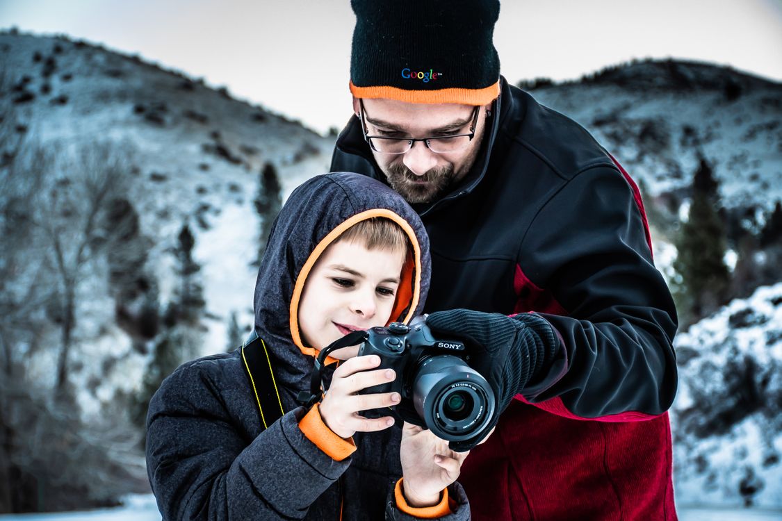 Man Standing Beside Boy While Holding Dslr Camera in Selective Focus Photography