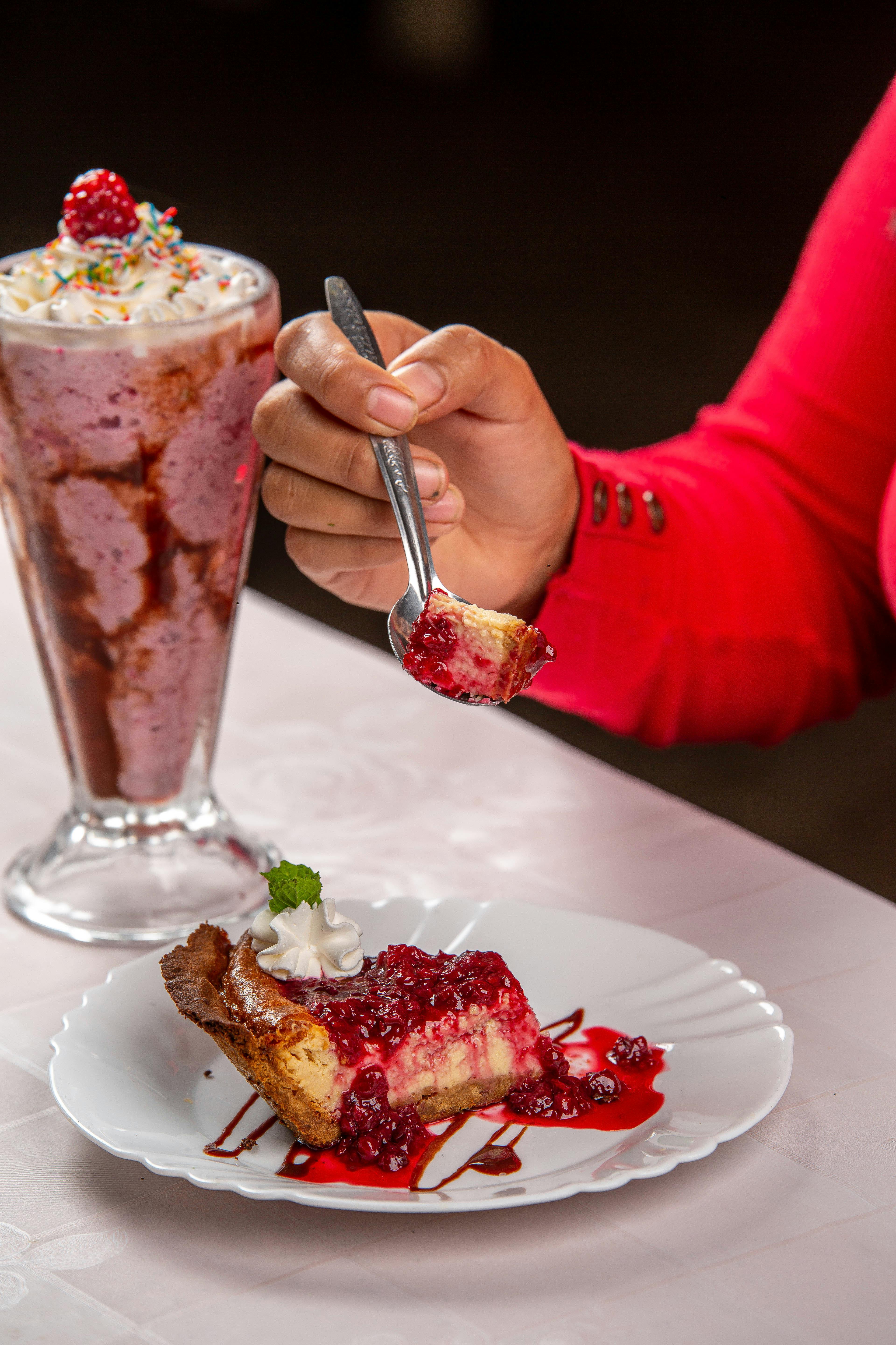 Close-up of berry cheesecake slice and milkshake being enjoyed indoors.