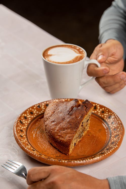 Hands Picking up Coffee Cup next to Plate of Yeast Cake