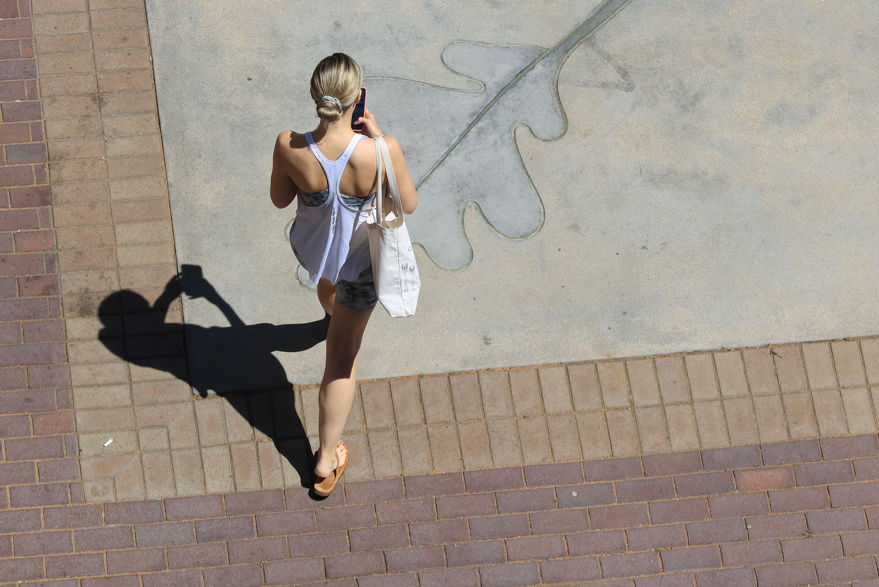 Aerial view of a woman walking on a sunlit pavement, casting a distinct shadow.