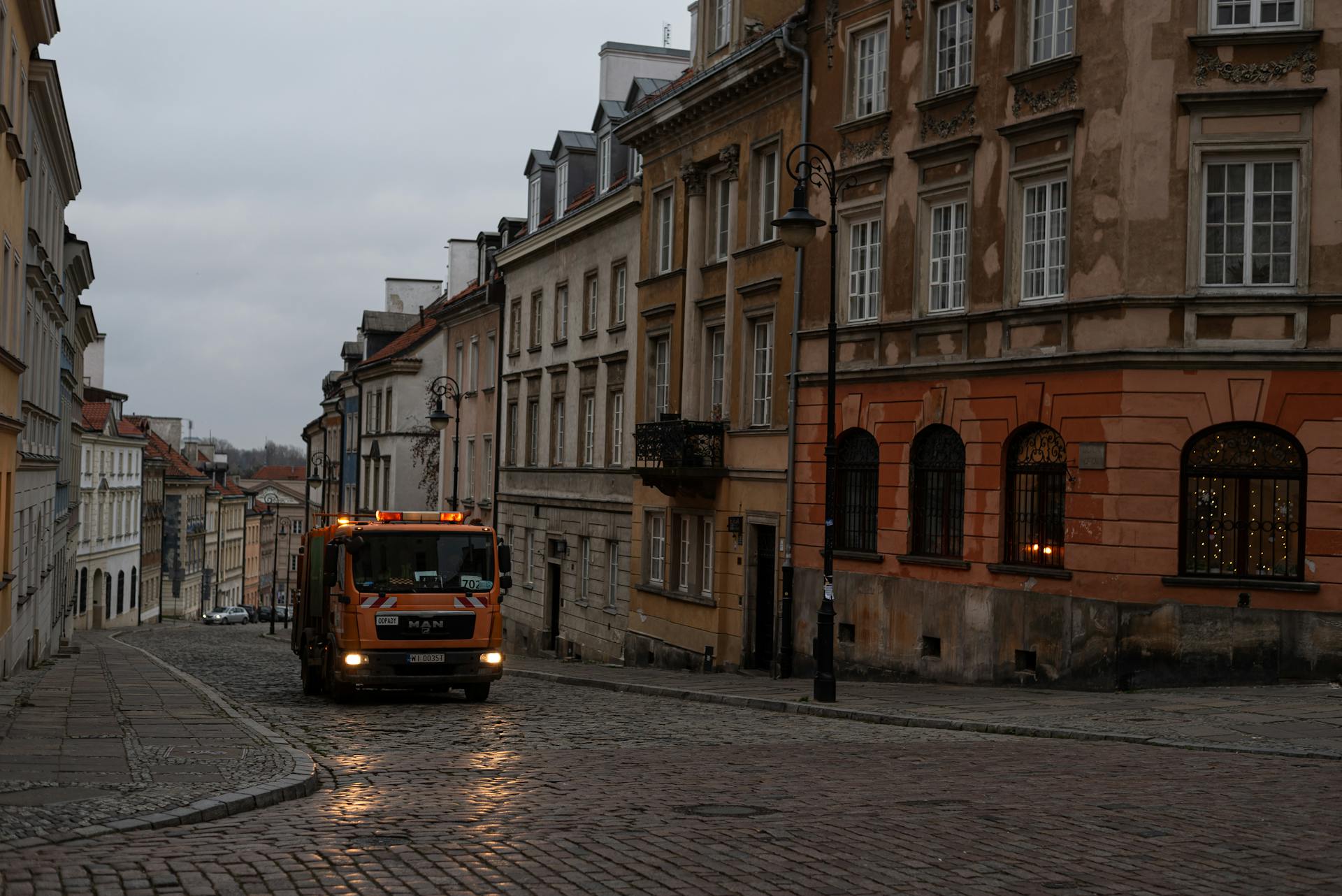 A peaceful street scene in Warsaw's old town with a garbage truck on a cobblestone street at dawn.
