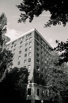 A black and white photo of a corner residential building surrounded by trees in an urban setting.