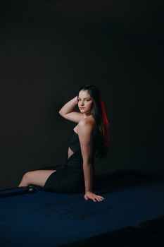 A woman in a black dress poses confidently on a billiard table, exuding elegance and glamour.