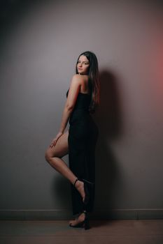 Stylish woman in black dress posing against a gray background indoors.