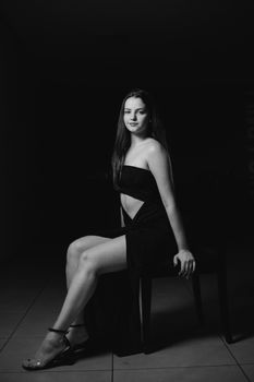 Black and white fashion portrait of a woman in elegant attire sitting on a chair, exuding grace and sophistication.