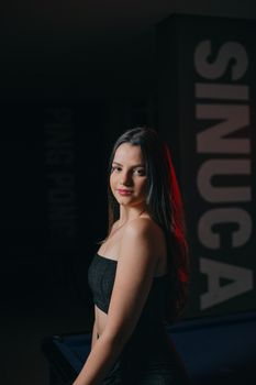 Stylish woman in a black dress posing elegantly at a billiard table indoors.