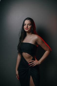 Confident young woman posing in a stylish black dress in a studio setting.