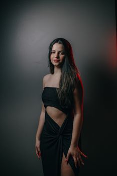 Fashion portrait of a woman in a stylish black dress posing elegantly against a gray background.
