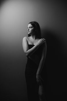 Black and white portrait of a woman in an elegant black dress in a studio setting.