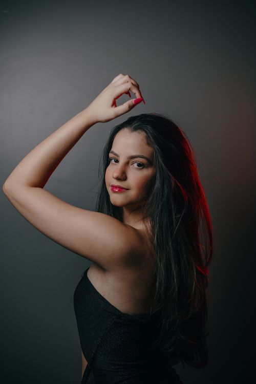 Free Portrait of a young woman posing elegantly in a studio setting with dramatic lighting. Stock Photo
