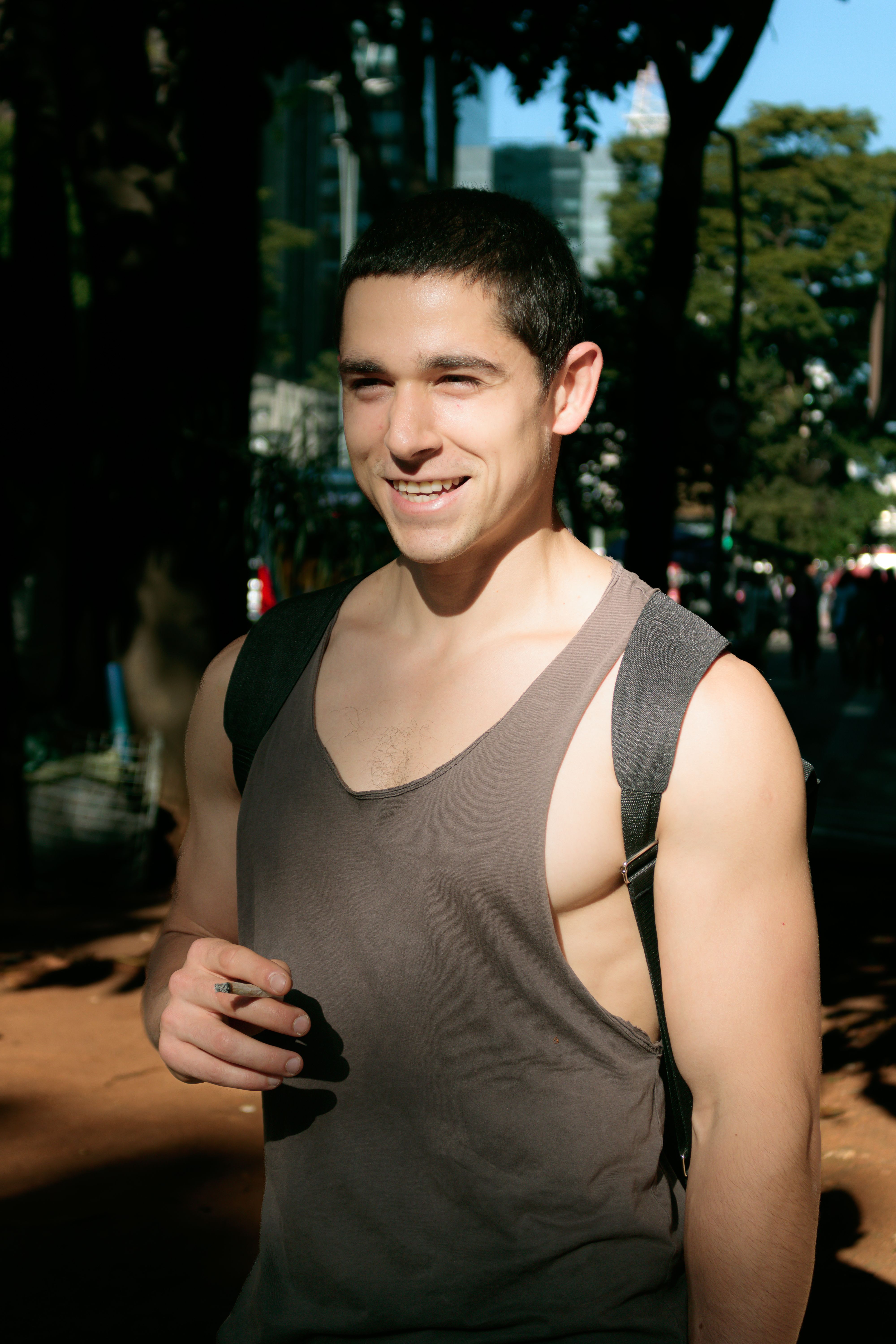 Smiling young man outdoors, wearing tank top, enjoying a sunny day in the city.