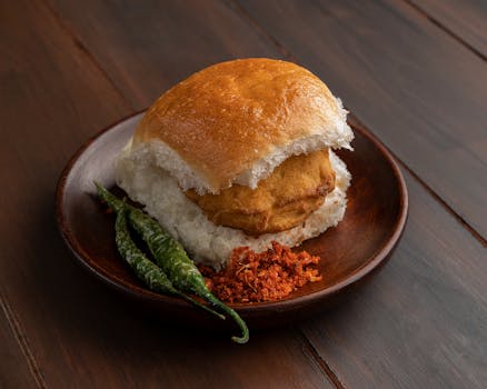 A mouthwatering Vada Pav served with green chili and chutney on a wooden plate.