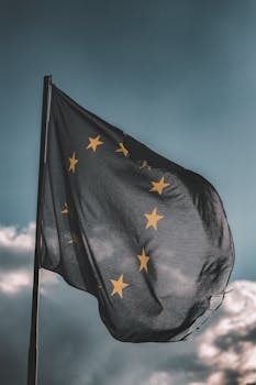 European Union flag gently waving on a flagpole against a cloudy sky, symbolizing unity and patriotism.