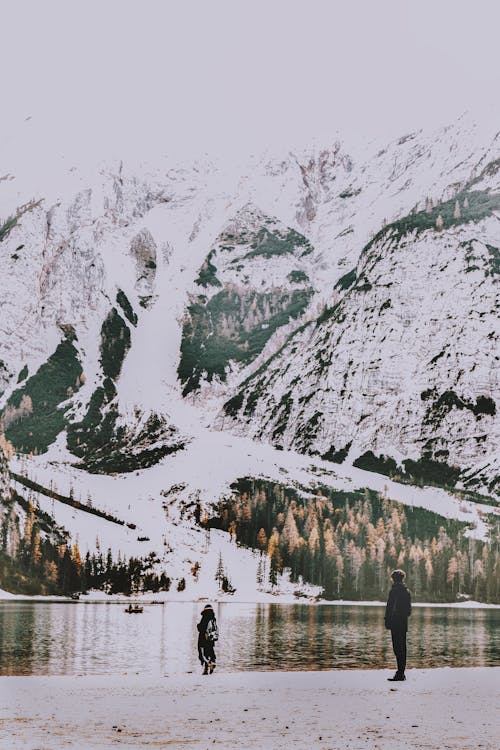 两人站在岸上俯瞰水和雪覆盖的山体