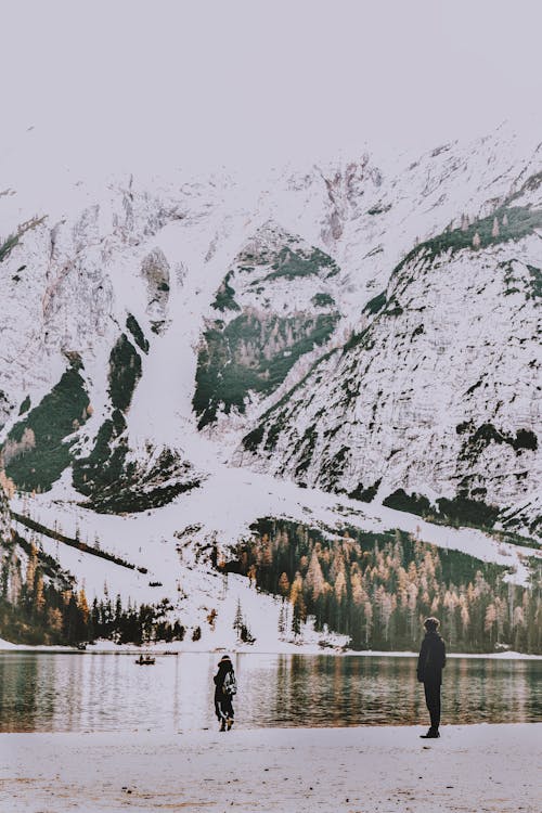 Zwei Leute, Die An Der Küste Stehen, Die Körper Des Wassers Und Des Schneebedeckten Berges überblicken