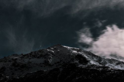Free Serene snow-covered mountain under a starry night sky, captured in a dramatic and moody setting. Stock Photo