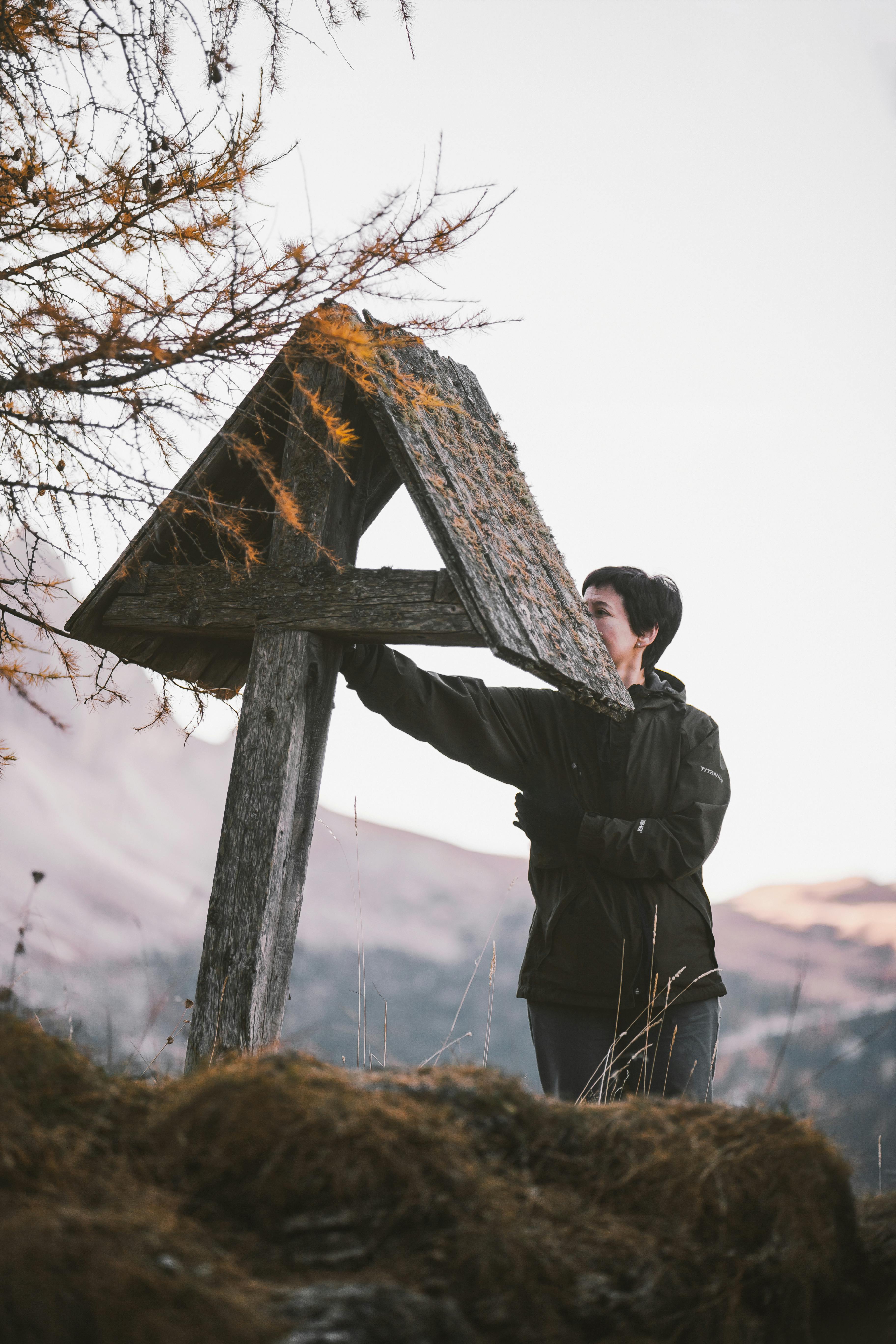 一名成年妇女在雾气缭绕的山间，与一块饱经风霜的木制标牌互动