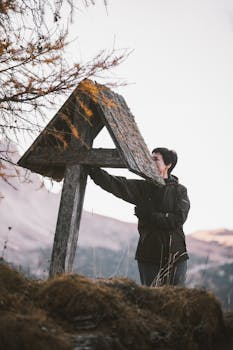 一名成年妇女在雾气缭绕的山间，与一块饱经风霜的木制标牌互动