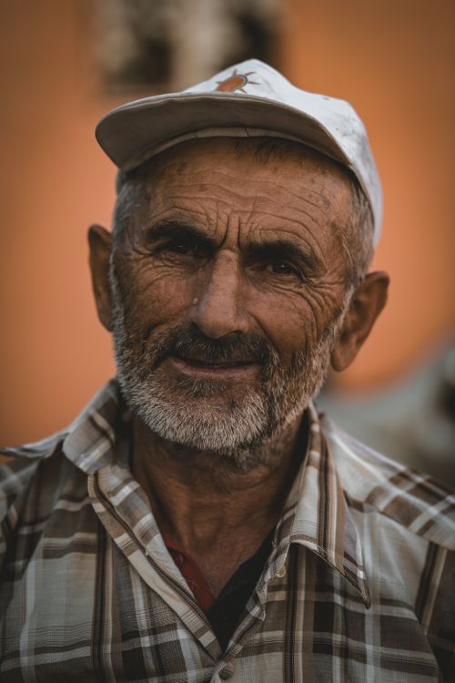Free Close-up portrait of an elderly man with gray hair and a mustache, wearing a checkered shirt and cap, smiling warmly. Stock Photo