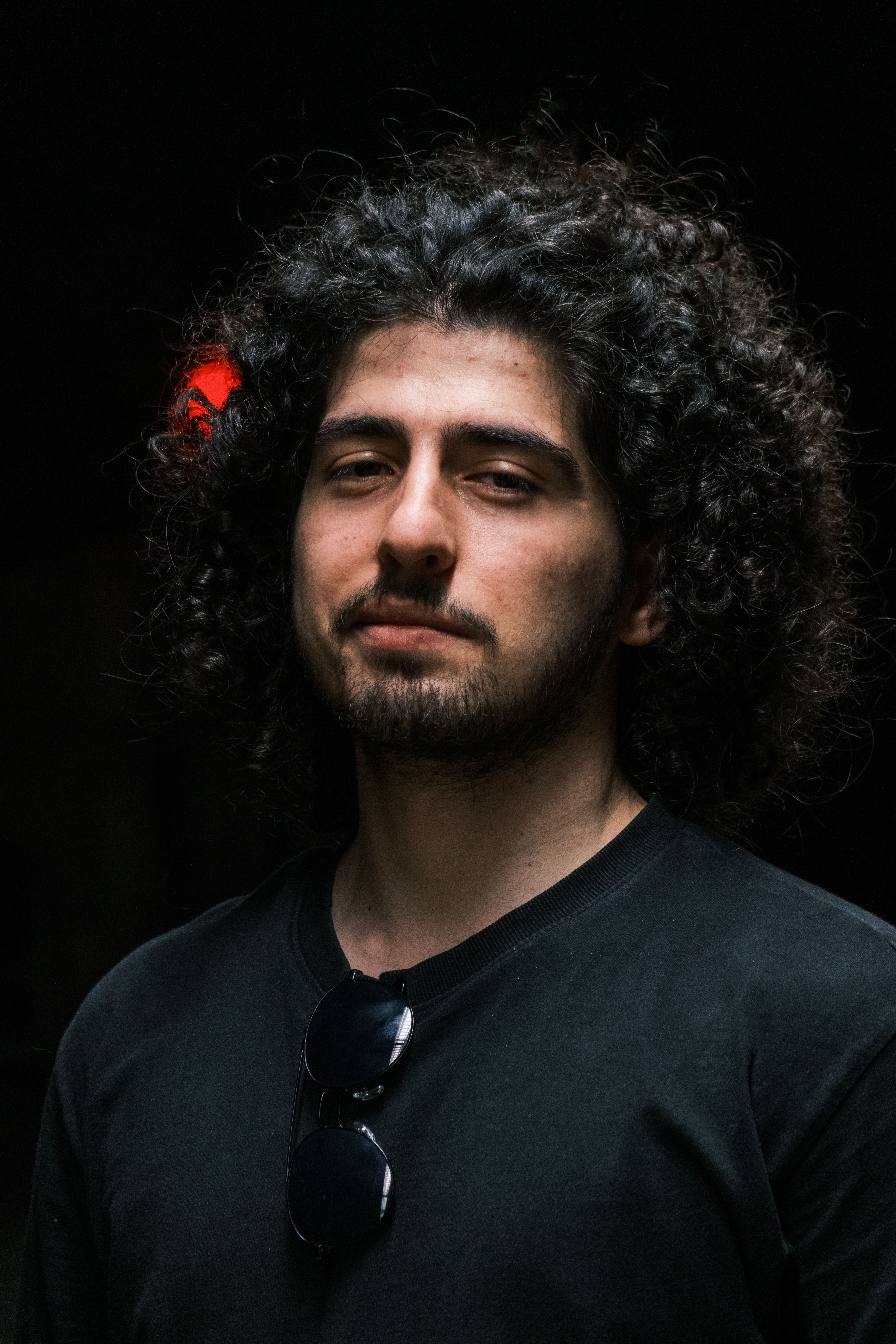 Portrait of a confident man with curly hair, wearing a dark shirt and sunglasses indoors.