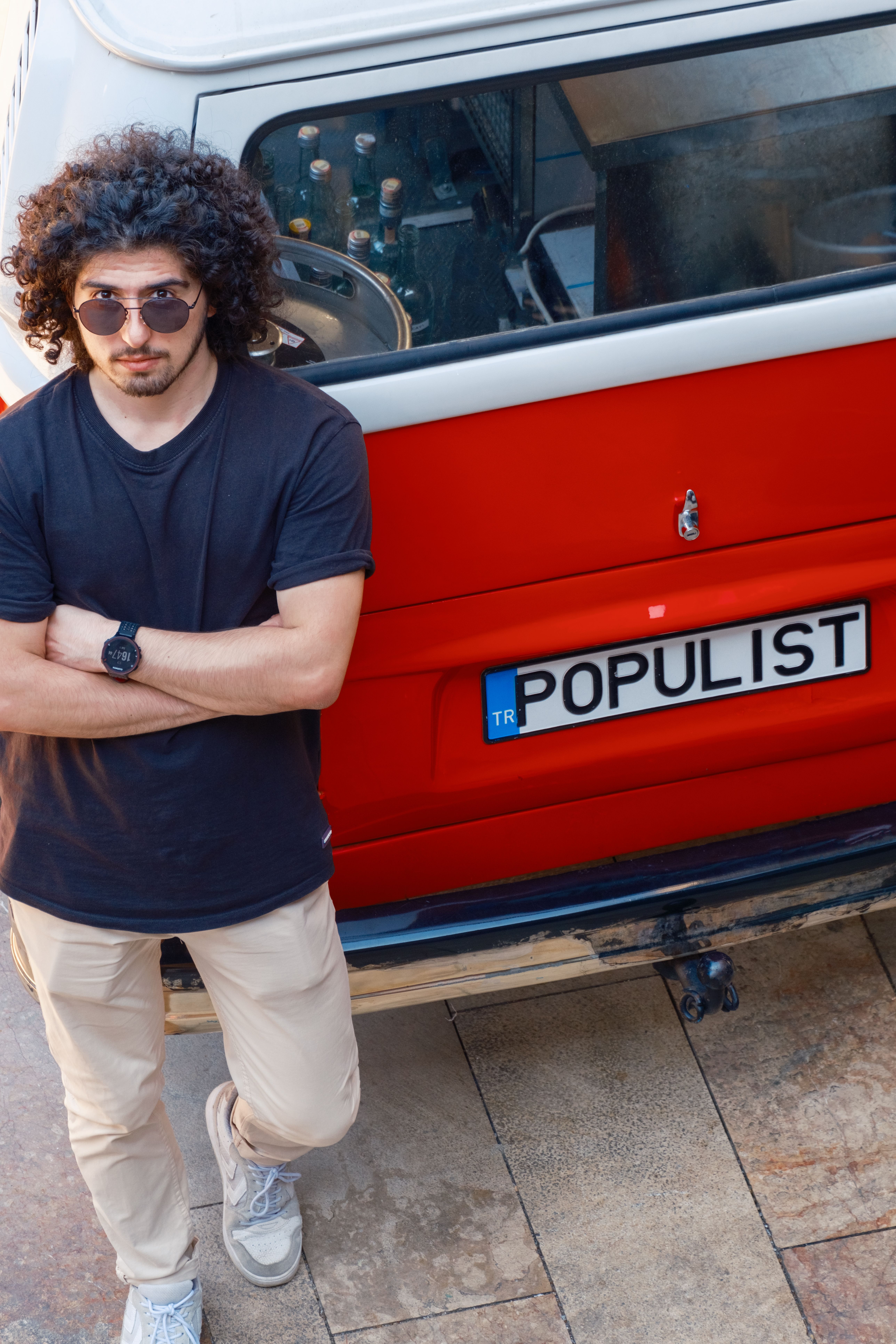 Confident man in sunglasses standing beside a red Volkswagen van in an outdoor setting.