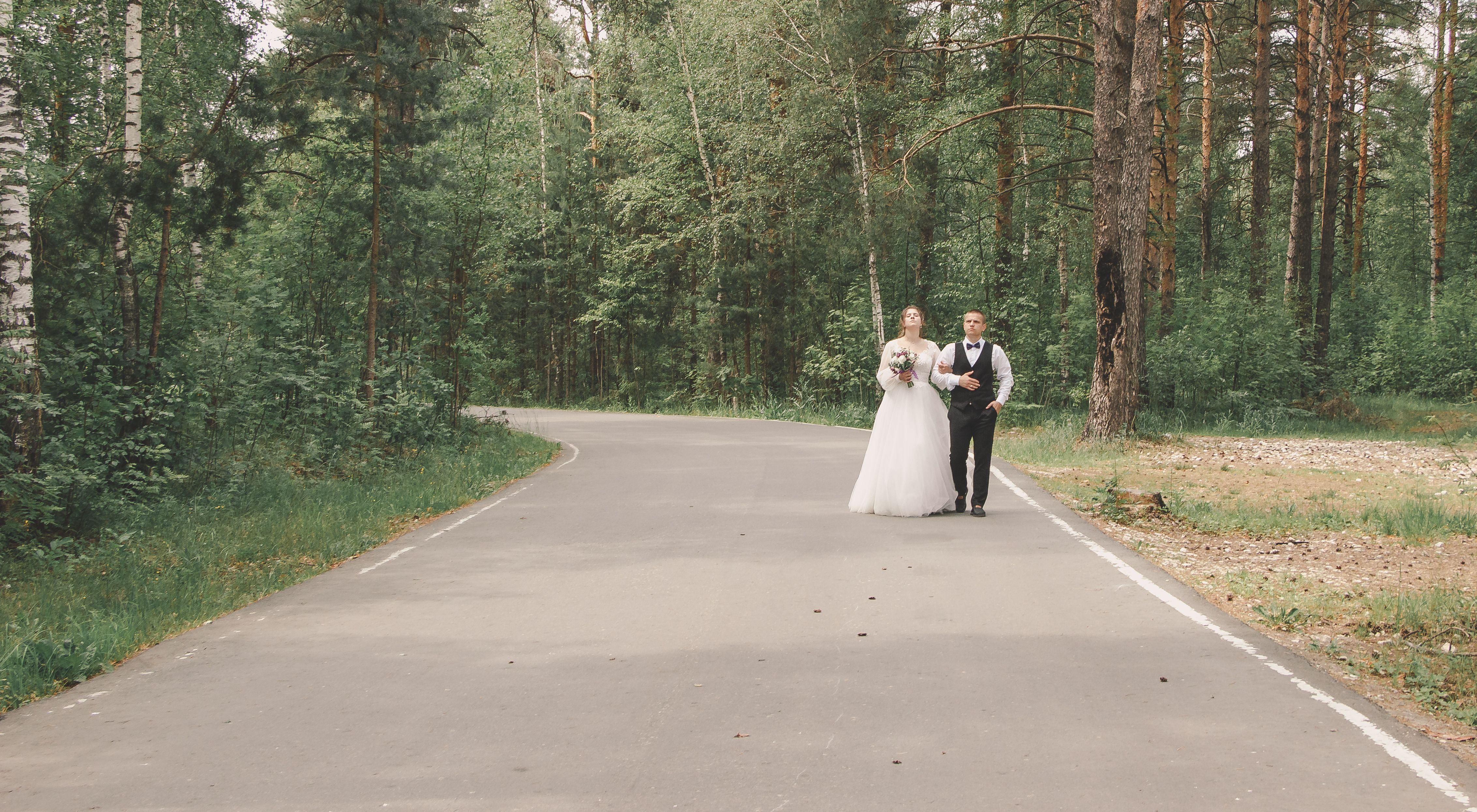 Bride and groom walking on a forest road during their wedding photo shoot.