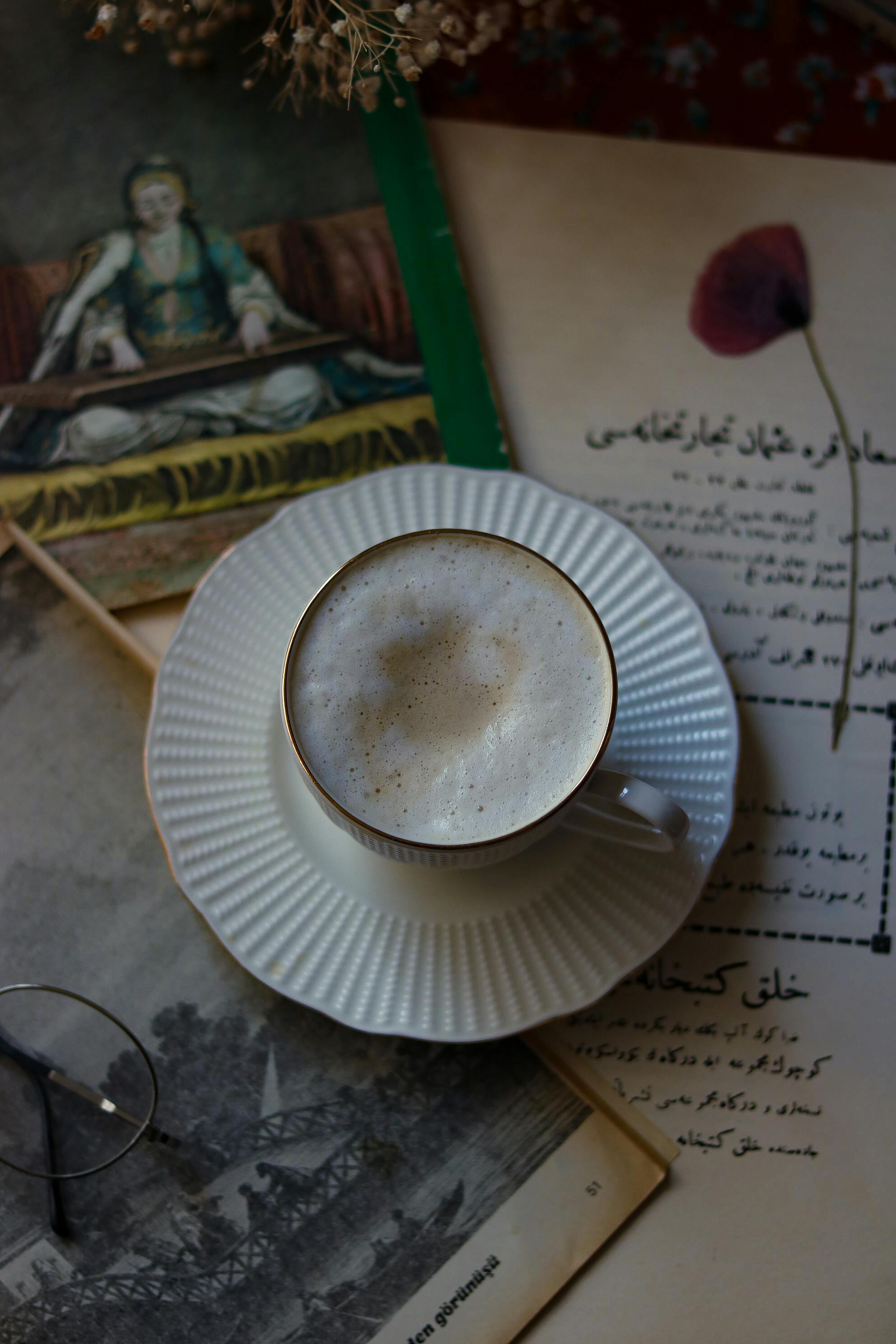 Elegant coffee cup with frothy cappuccino on vintage books and art in a cozy setting.