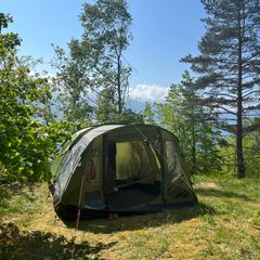 An olive green tunnel tent with its door open on a sunny hillside