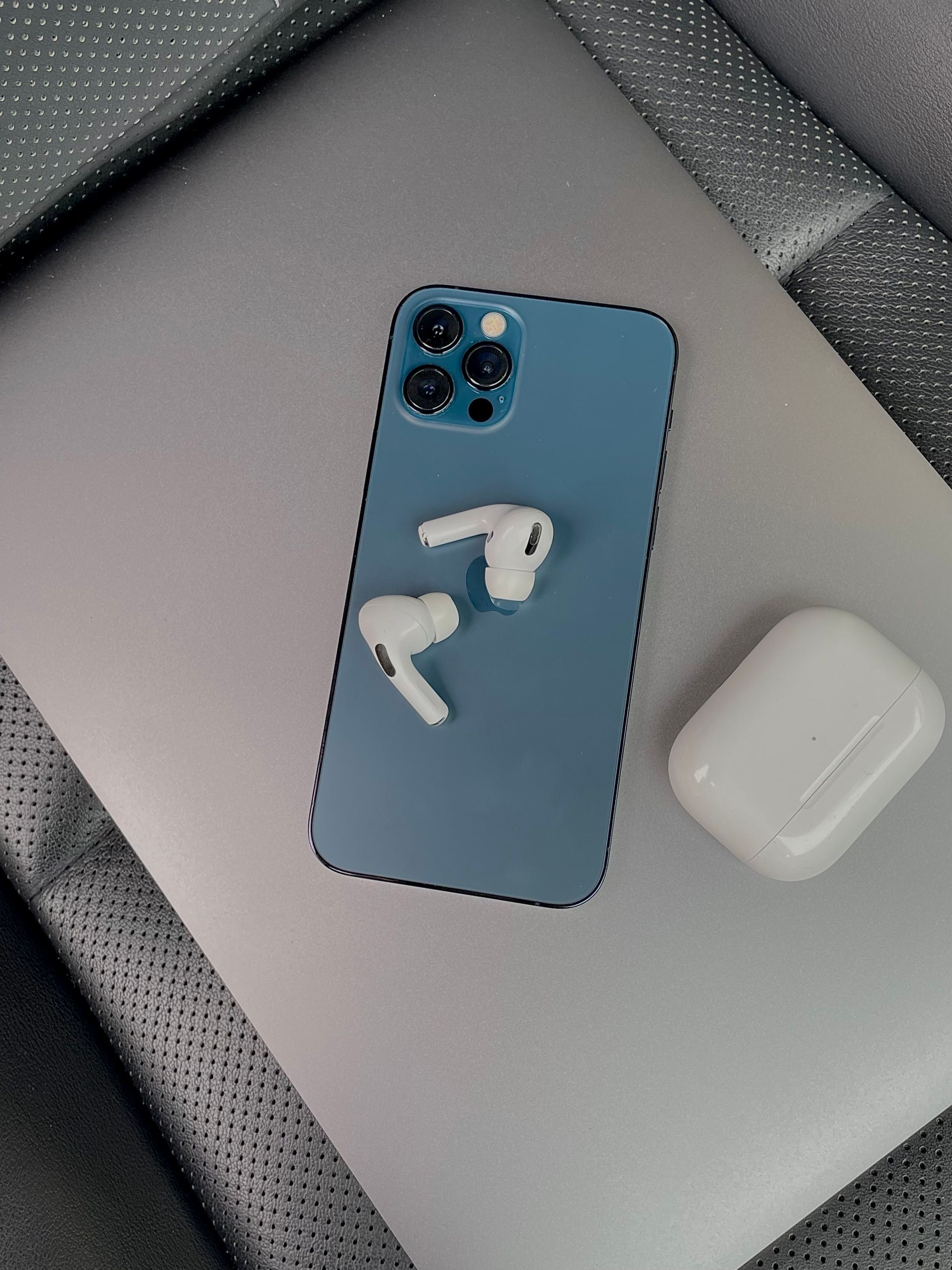 Blue smartphone with earbuds and charging case on leather surface, showcasing modern technology.
