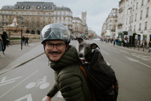 Man on bicycle with a dog in a backpack, smiling on a Parisian street.